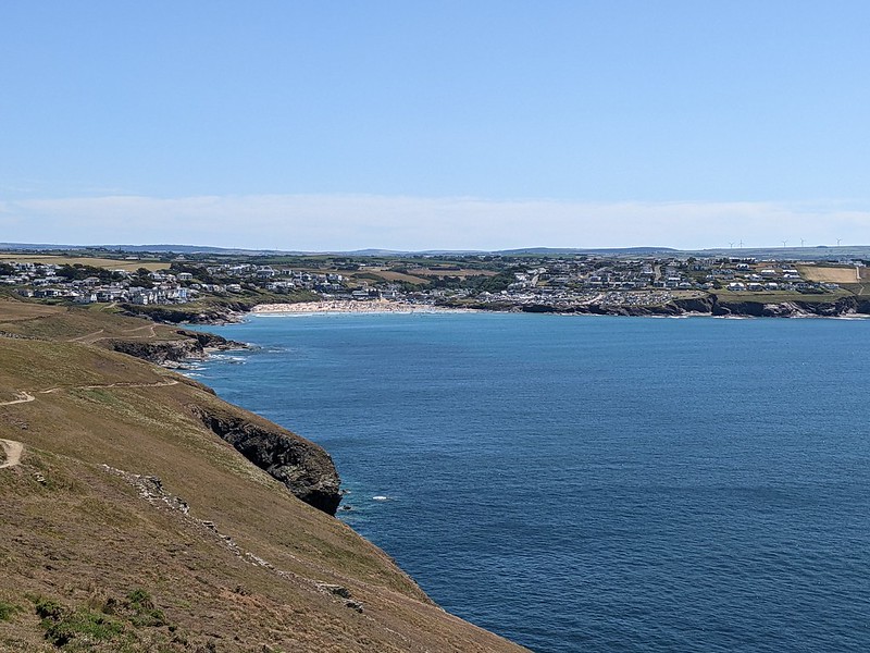 View of Polzeath beach in the distance with the Atlantic in the foreground and the cliffs to the left. 