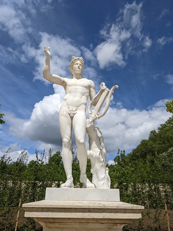 White statue of a man holding a harp, against a blue sky. 