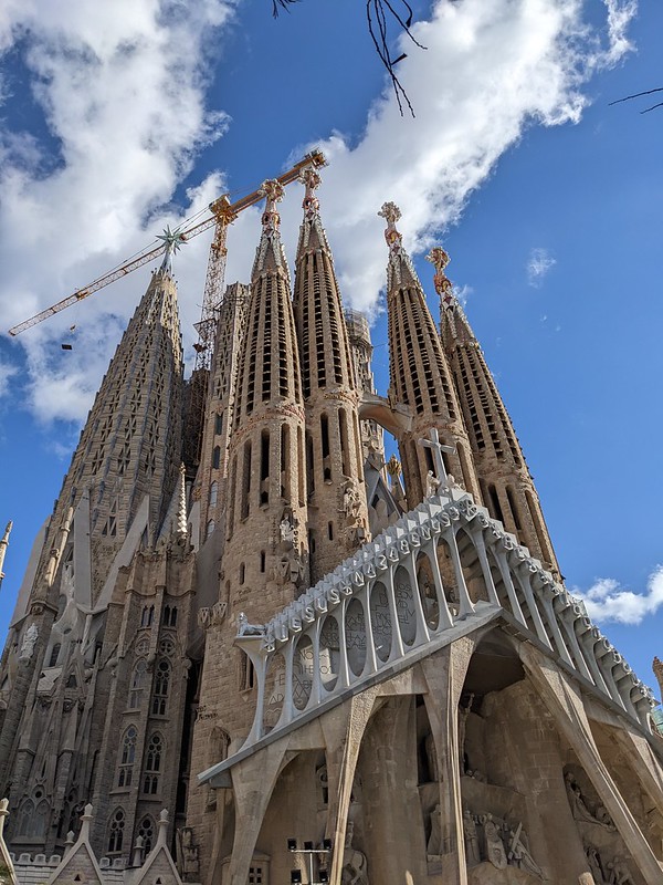 Looking up at the Sagrada Familia with a crane working on it under the blue sky