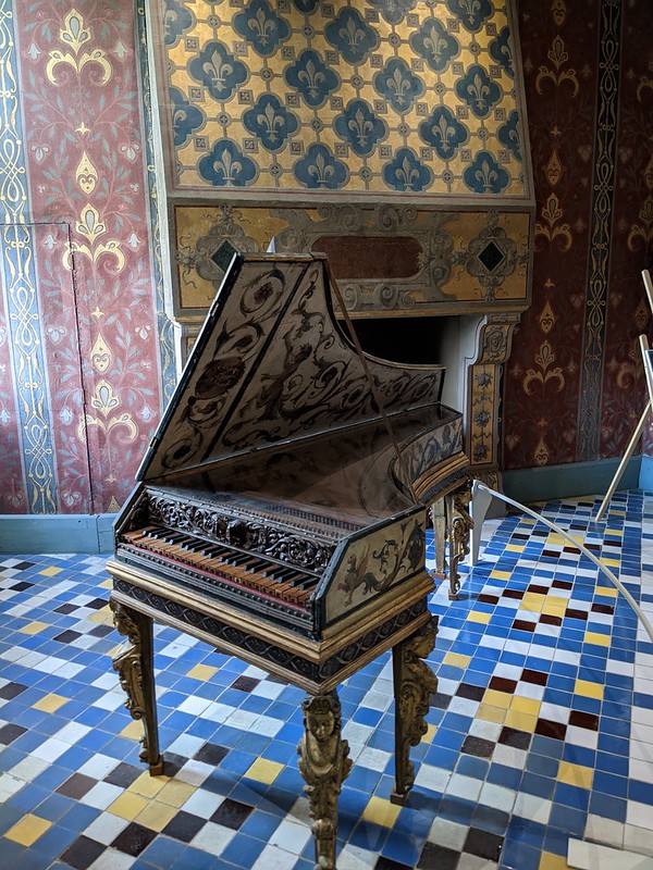 Old wing piano, not full size, against the blue tiled flour and red walls.