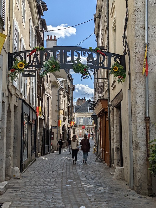 Narrow street between old houses with a sign across the top reading "Quartier des arts" (in french).