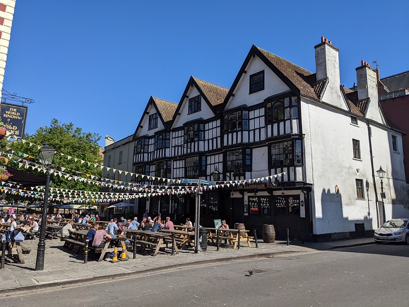 Pub goers sitting on benches outside The Llandoger Trow under sunny blue sky