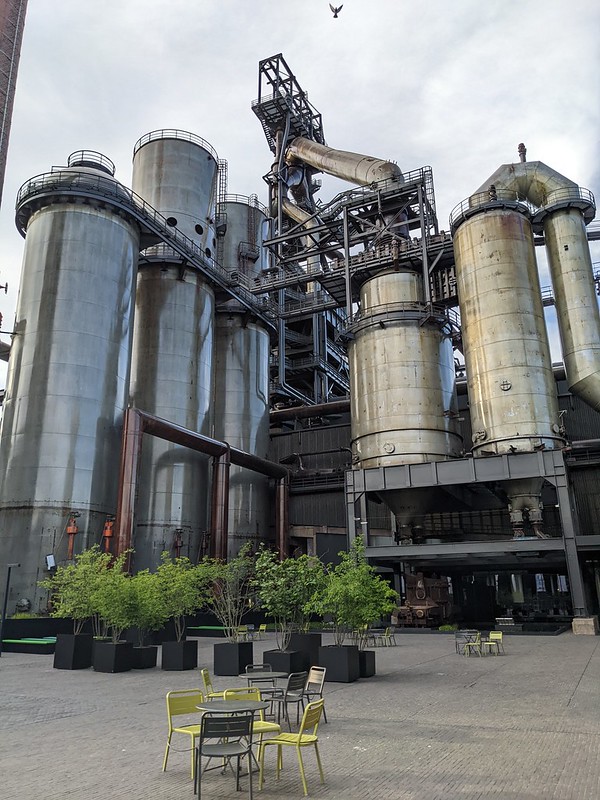 Huge grey pipes of the steelworks overlooking a green coffee table