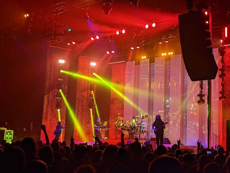 Dream Theater on stage against a red backdrop with several yellow search lights flooding the stage