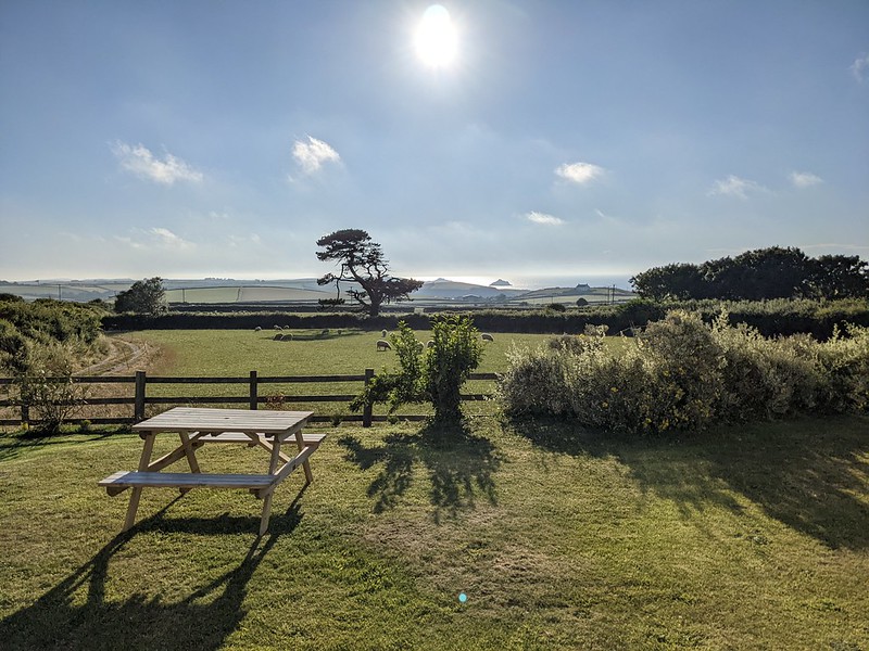 View of the see in the distance with a picnic bench in the foreground in the late afternoon sun