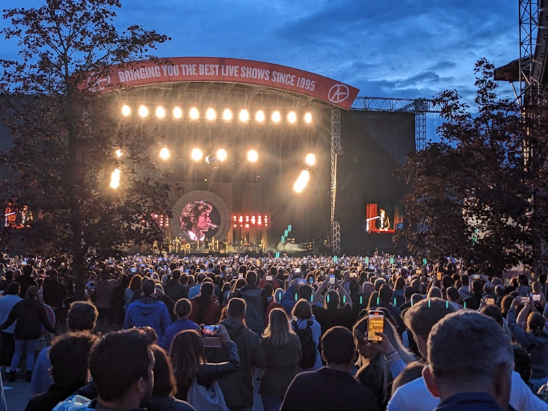 Arctic Monkeys on stage in the fading light with the spotlights on full power pointing at the crowd.