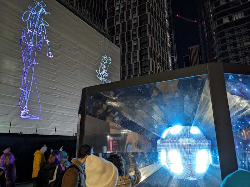 Line drawn figures projected on a large screen provided by a building in construction with a neutron exhibit in the foreground