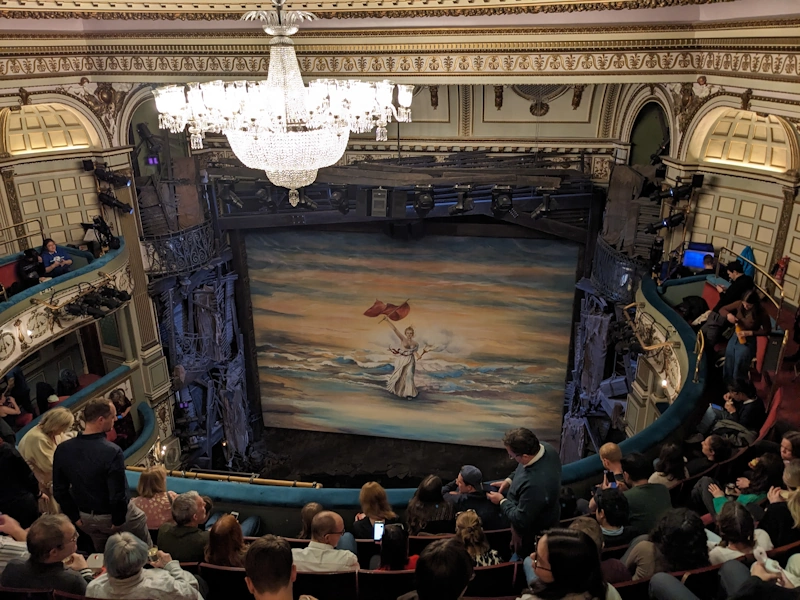 Interval scene of Les Miserables with lady dressed in white waving large red revolutionary flag in front clouds lit up by sunset