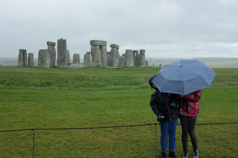 People with umbrellas standing in front of stonehenge