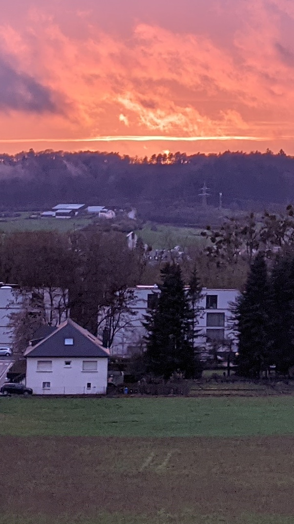 Sun setting behind the wooded hills on the other side of the valley creating a bright red sky just at the horizon.