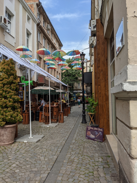Small lane with cafes and colourful umbrellas overhead providing shade.