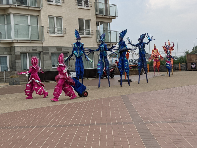 Performers dressed as sealife walking down the beach front on stilts