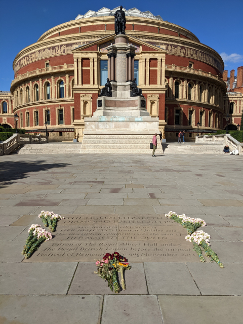 Flowers put alongside a commemorative plaque of the Queen, with the round Royal Albert Hall in the background.